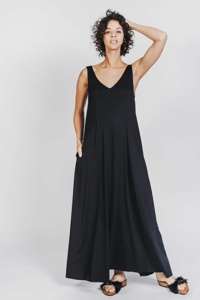 Deep White Black Modell SASHA langes Kleid schwarz mit schwarzen Fellsandalen aus Holz von Devich, ärmelloses Sommerkleid mit V-Ausschnitt, Ansicht gesamt von vorne