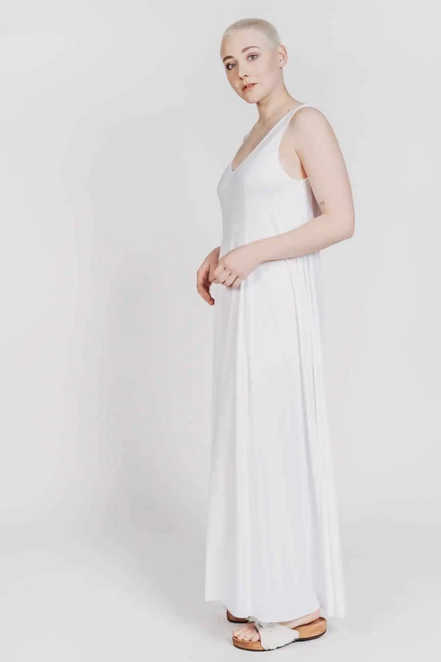 Deep White Black Modell SASHA langes Kleid weiß mit weißen Fellsandalen aus Holz von Devich, ärmelloses Sommerkleid mit V-Ausschnitt, Ansicht gesamt von links